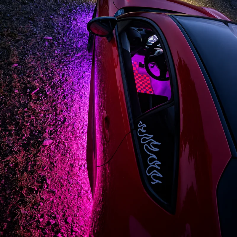 Červená Toyota GR86 s fialovým podsvícením podvozku a interiéru za šera